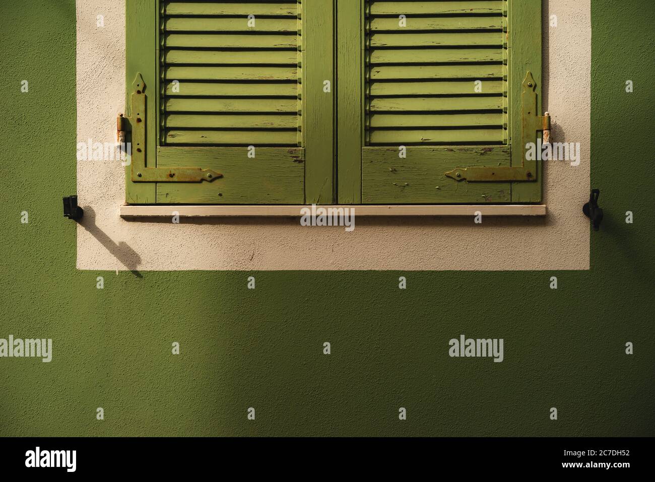 Closeup shot of green, wooden window shutters outlined with white on a green wall Stock Photo