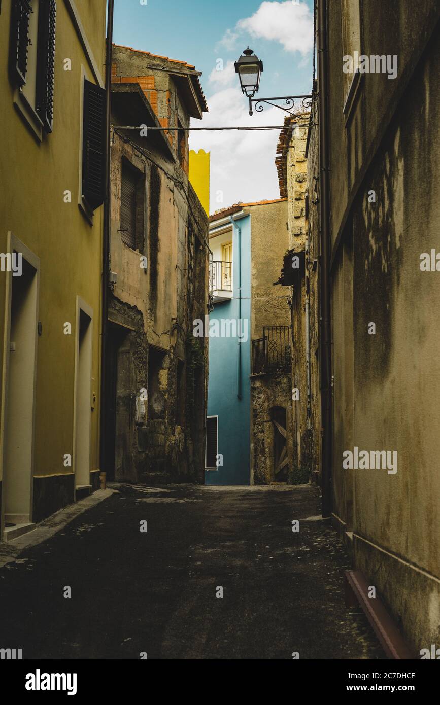 Vertical shot of an empty alley aligned with old yellow buildings leading to a blue building Stock Photo