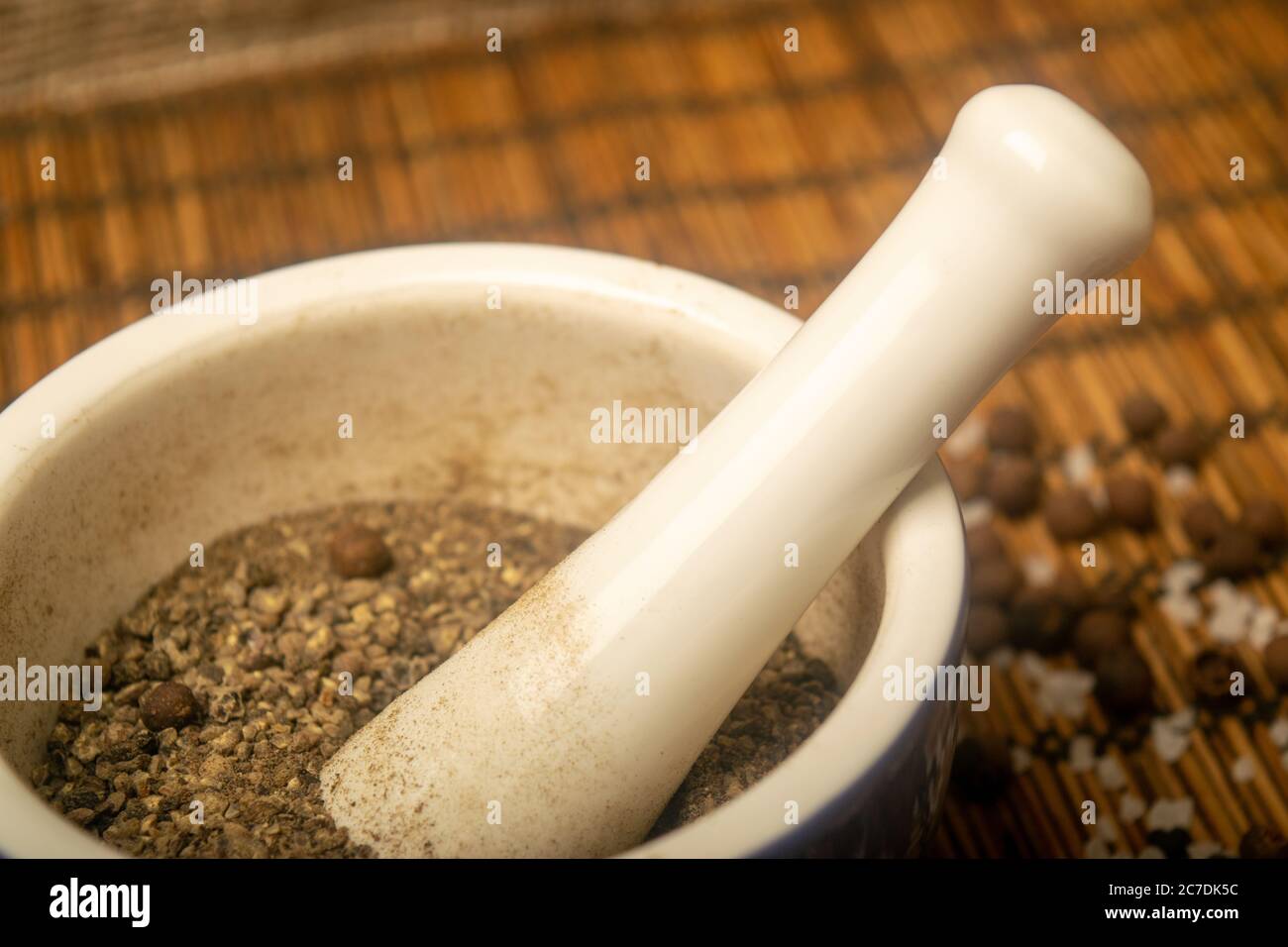 Ground black allspice in a ceramic mortar and black allspice and coarse salt scattered on a reed Mat. Close up Stock Photo