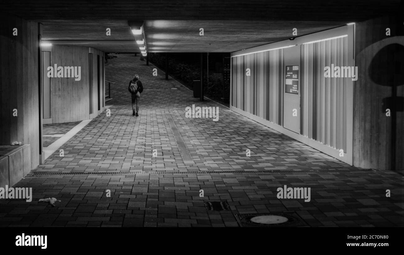 Beautiful shot of a person walking on an alleyway in the middle of a building sin black and white Stock Photo