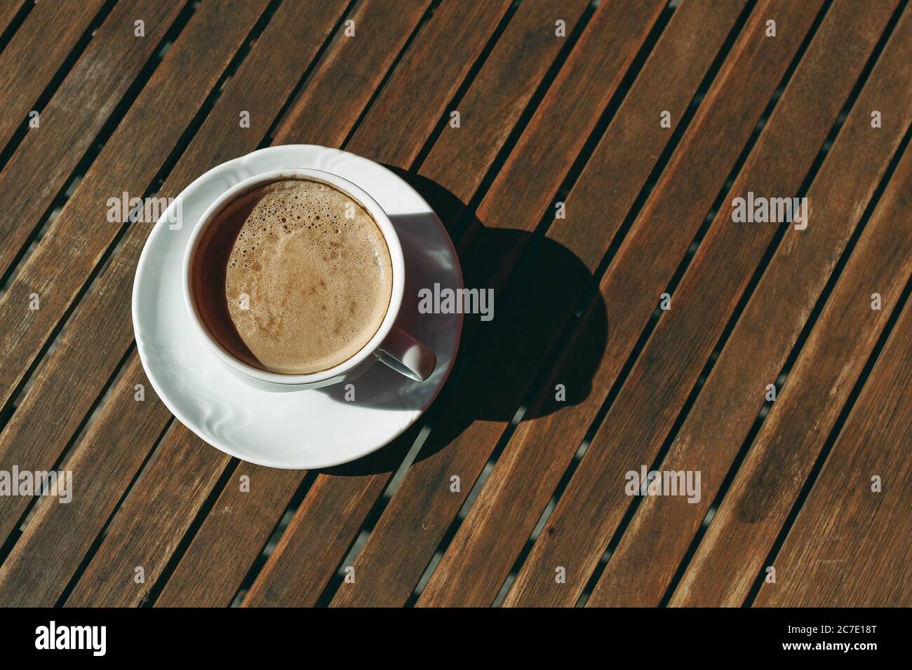 White cup of cappucino coffee in sunlight with harsh shadows on old wooden table background. Breakfast, break concept. Flat lay, top vie. No people Stock Photo