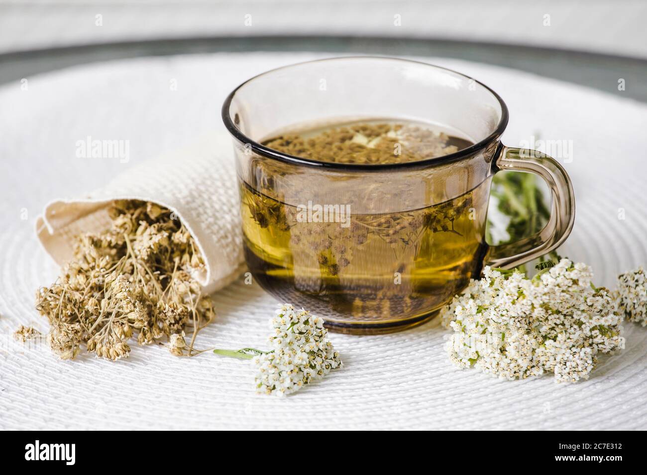 Still life of Achillea millefolium, yarrow or common yarrow herbal medicinal tea in glass with dry tea powder and fresh blossoms on white minimal set Stock Photo
