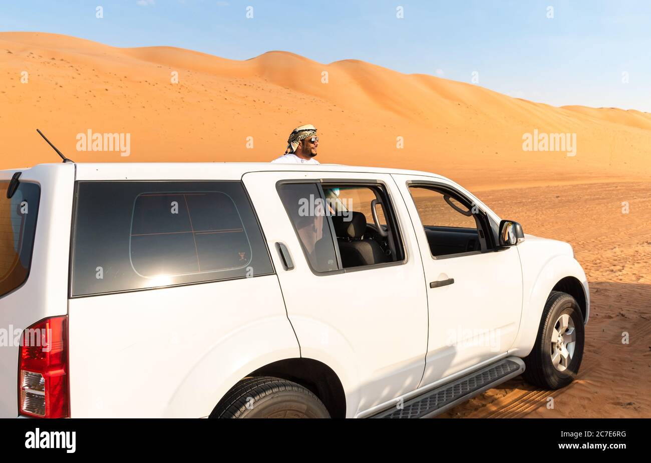 Wahiba Sands, Oman - February 12, 2020: The white 4x4 off-road car with Omani man in traditional cloth in Wahiba Sands Desert, Sultanate of Oman. Stock Photo