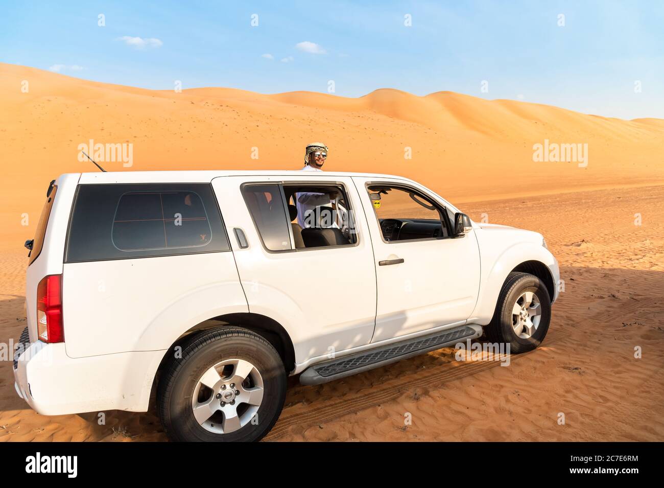 Wahiba Sands, Oman - February 12, 2020: The white 4x4 off-road car with Omani man in traditional cloth in Wahiba Sands Desert, Sultanate of Oman. Stock Photo