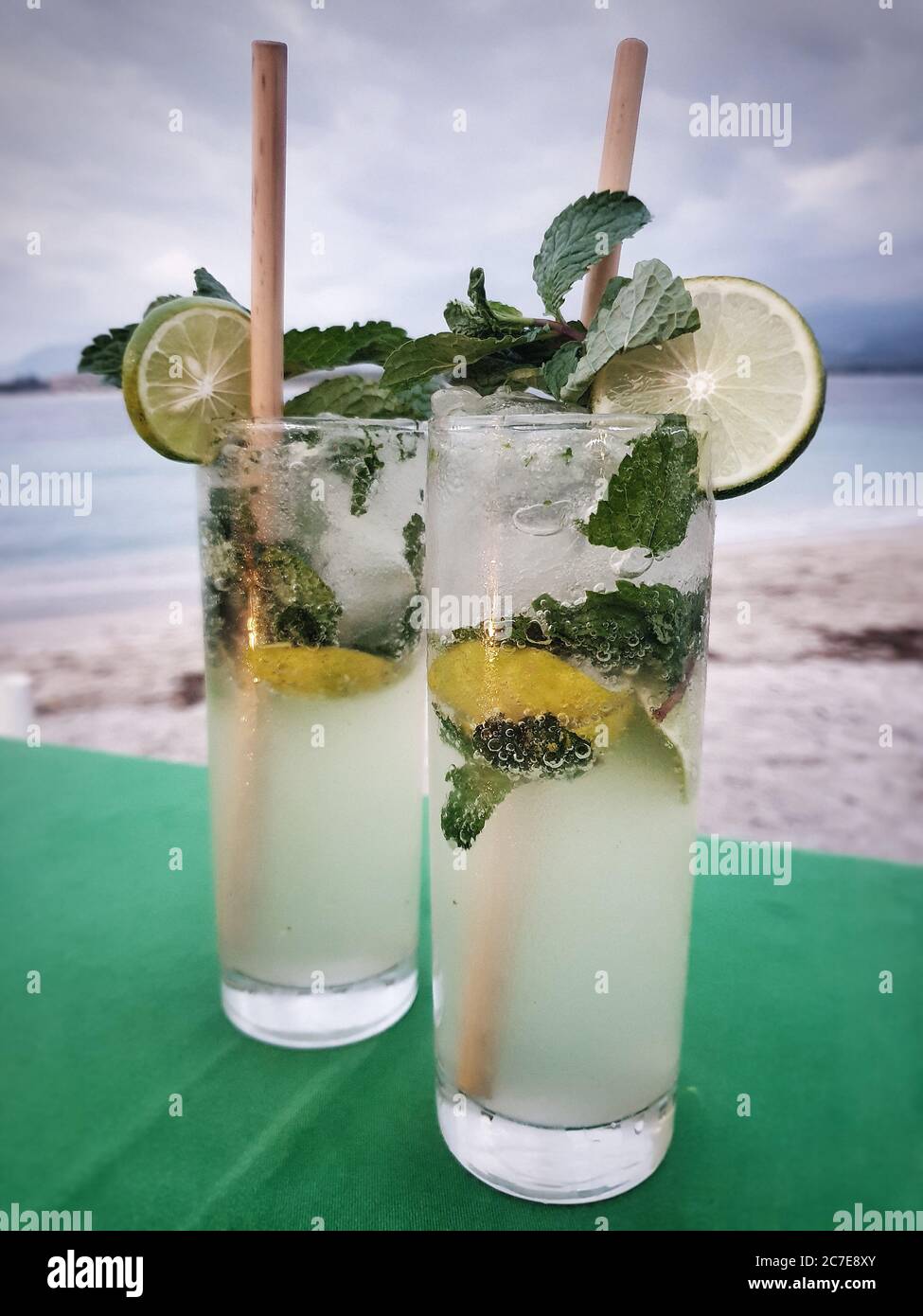 Close up of two mojitos in tall glasses with wooden straws on a green table on a beach in Indonesia Stock Photo