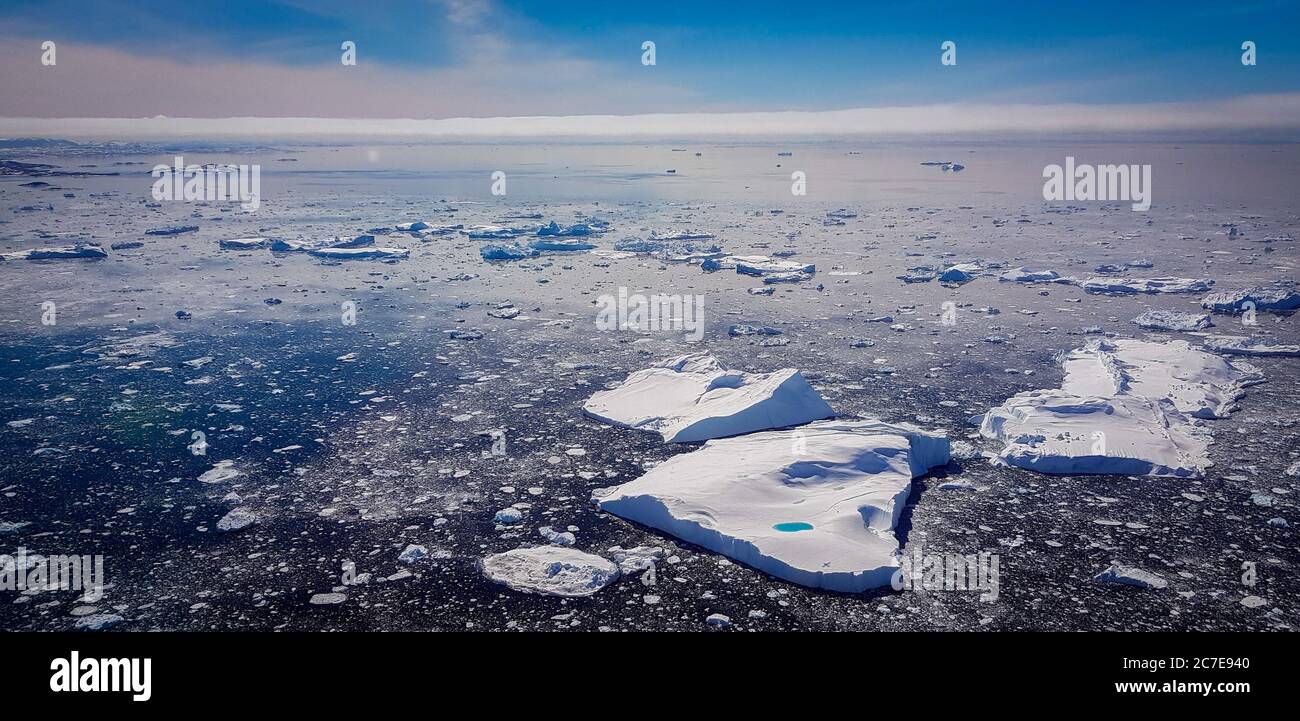 Aerial shot of icebergs and sea ice scattered across the mouth of a fjord Stock Photo