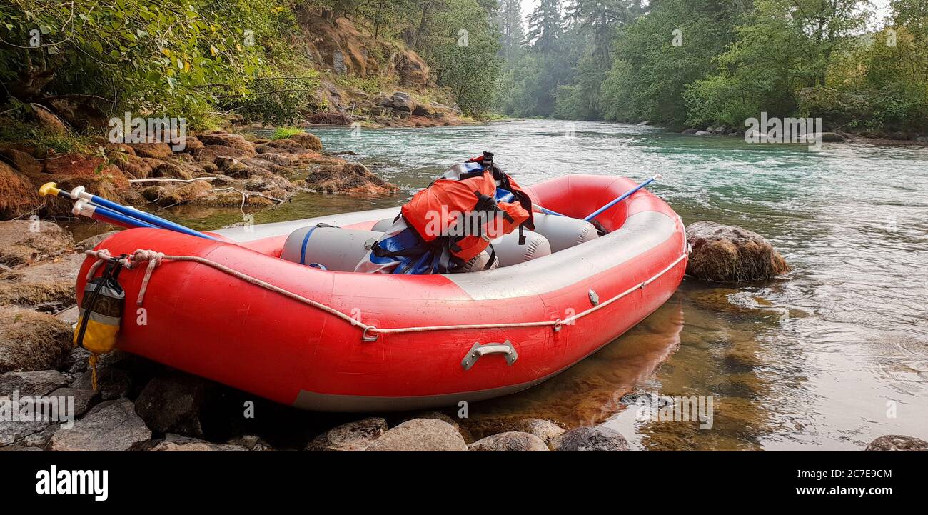 Red raft on edge of beautiful river with backpack and ores resting inside Stock Photo