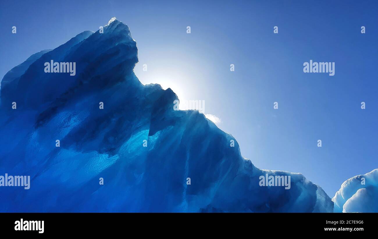 Sun behind beautiful glacial blue iceberg Stock Photo