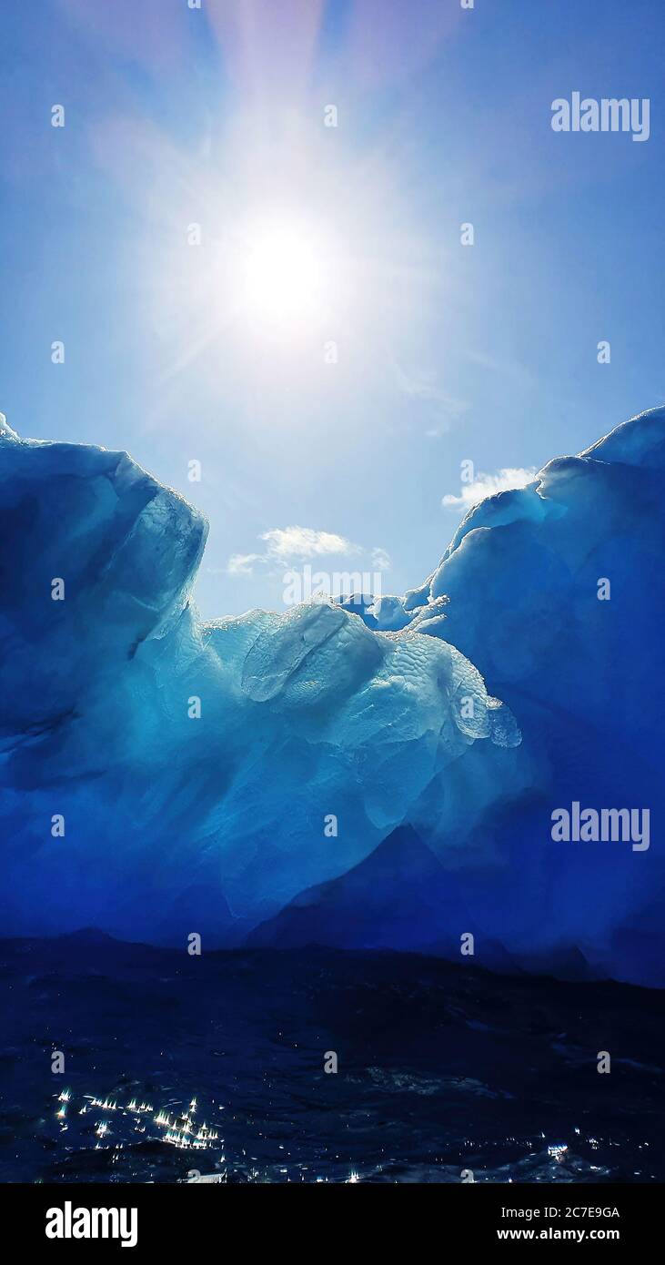 The sun shines above a glistening glacial blue iceberg in Antarctic waters Stock Photo