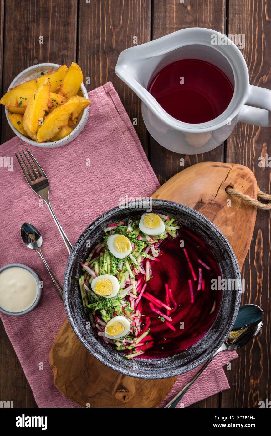 Cold beetroot soup with eggs, baked potatoes, souce, rustic wooden background, white jug, pink tablecloth, top view Stock Photo