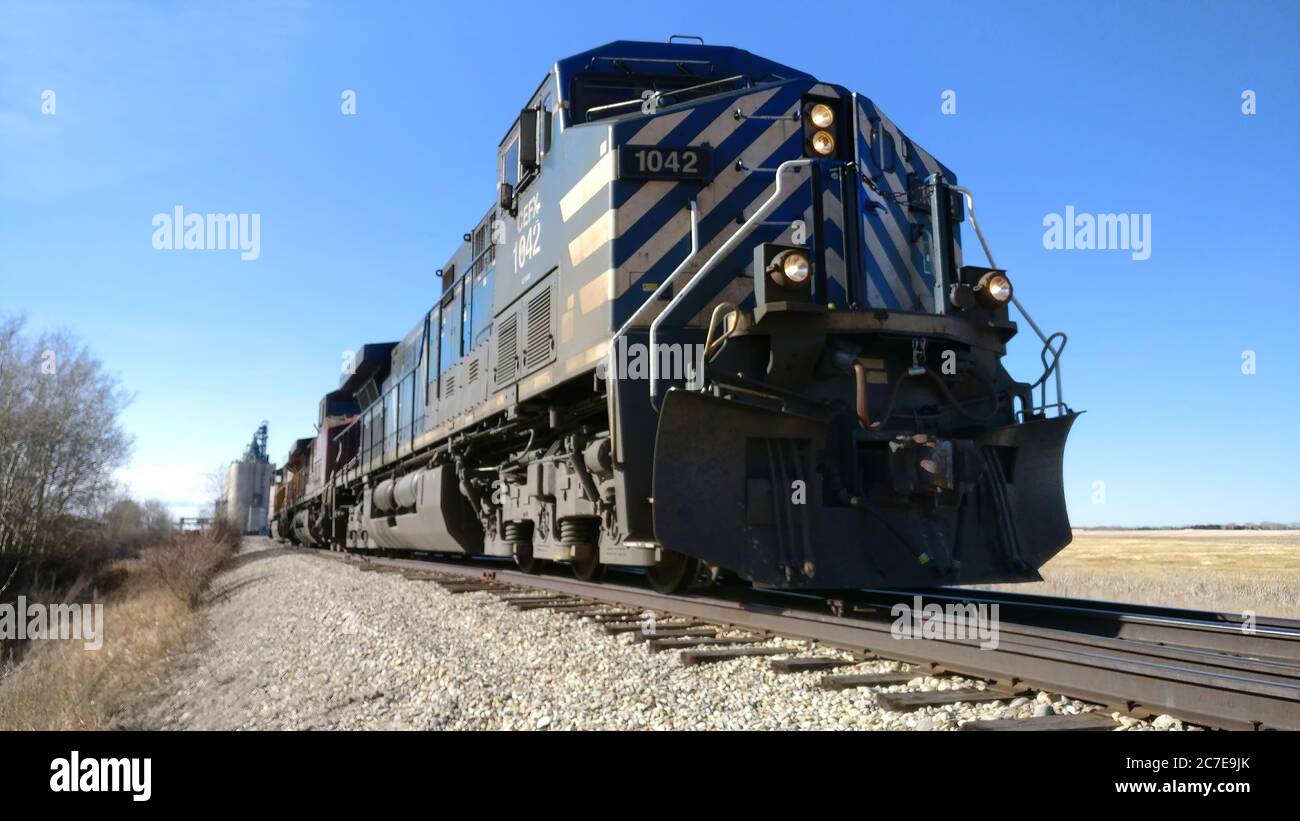Blue diesel train engine pulling grain cars away from a grain silo in arid fields Stock Photo