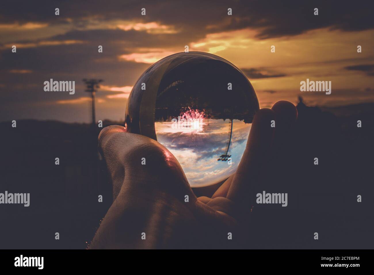 A person holding a glass ball with the reflection of colorful sky and ...