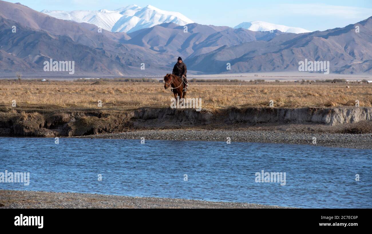 A nomadic Kazakh herder on horseback at the beginning of winter in the Altai Mountains, western Mongolia. Stock Photo
