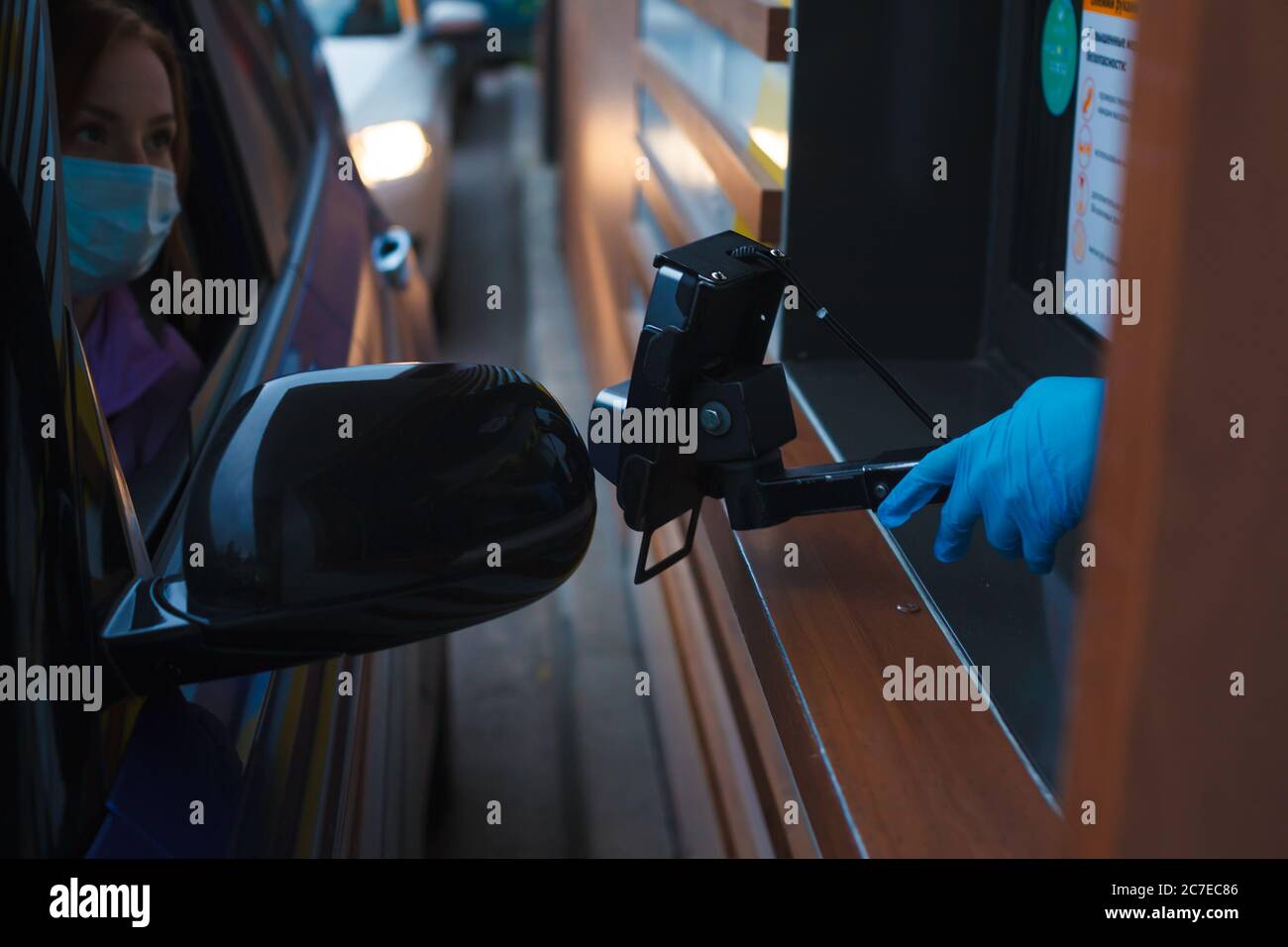 Waitress in takeaway window offering a payment terminal to woman in protective mask sittting in a car Stock Photo