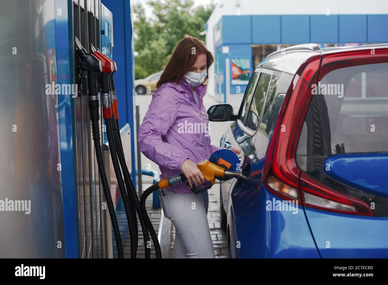 Woman in medicine mask filling car tank on a petrol station Stock Photo