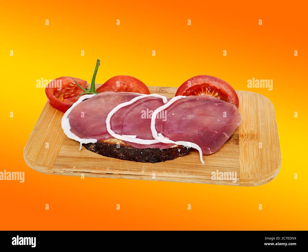 Ham bread on a wooden board, isolated against a orange background. Stock Photo