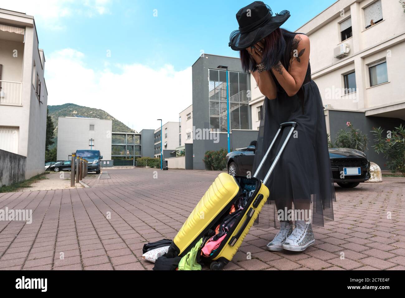 The angry woman trying to close the suitcase that suddenly opened on the road. Stock Photo
