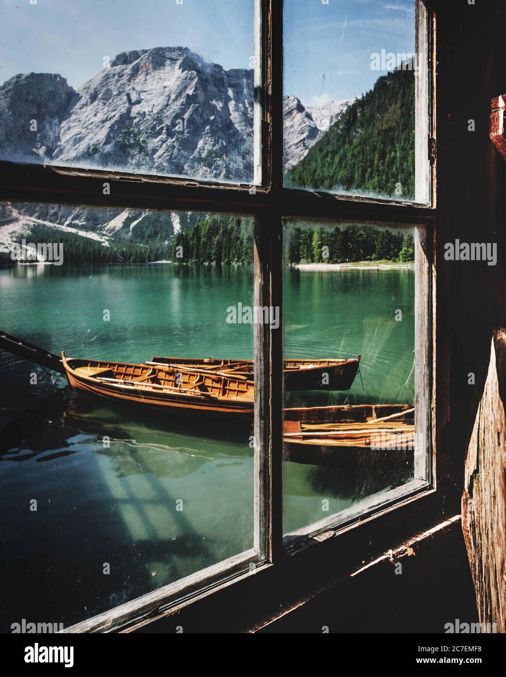 Vertical shot out of old window of wooden boats on peaceful Lake Prags Italy surrounded by mountains Stock Photo