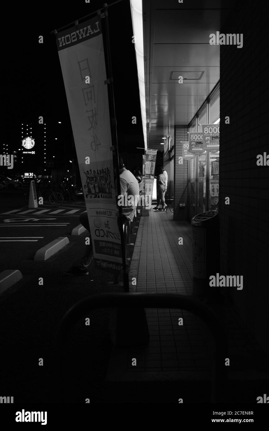 MATSUYAMA, JAPAN - Sep 23, 2019: A vertical greyscale shot of people on the street waiting for the bus at night Stock Photo