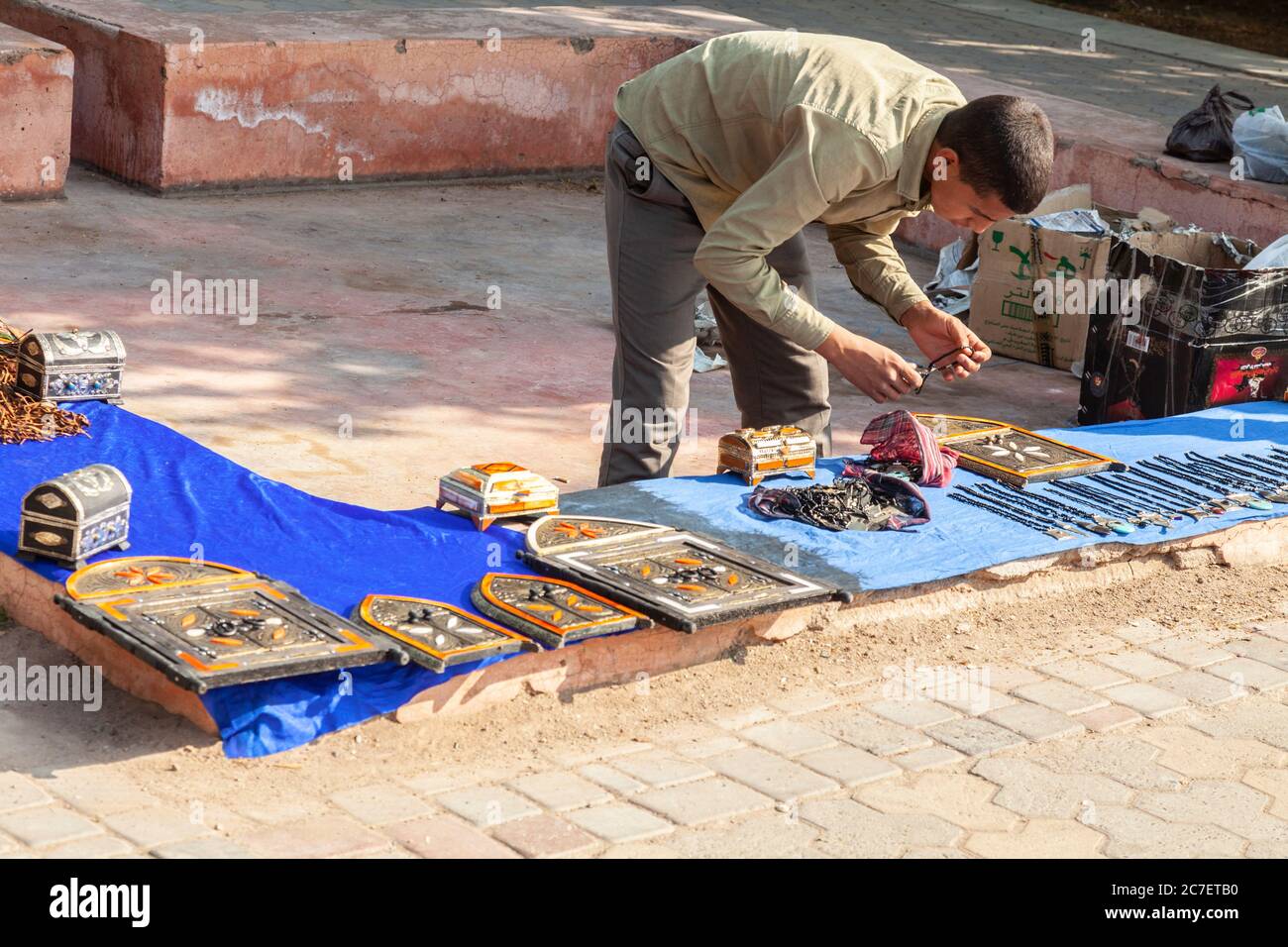 A young hawker sets out his goods for sale - pendants, caskets and placks representing doors - outside Kutubiyya Mosque in central Marrakech. Stock Photo