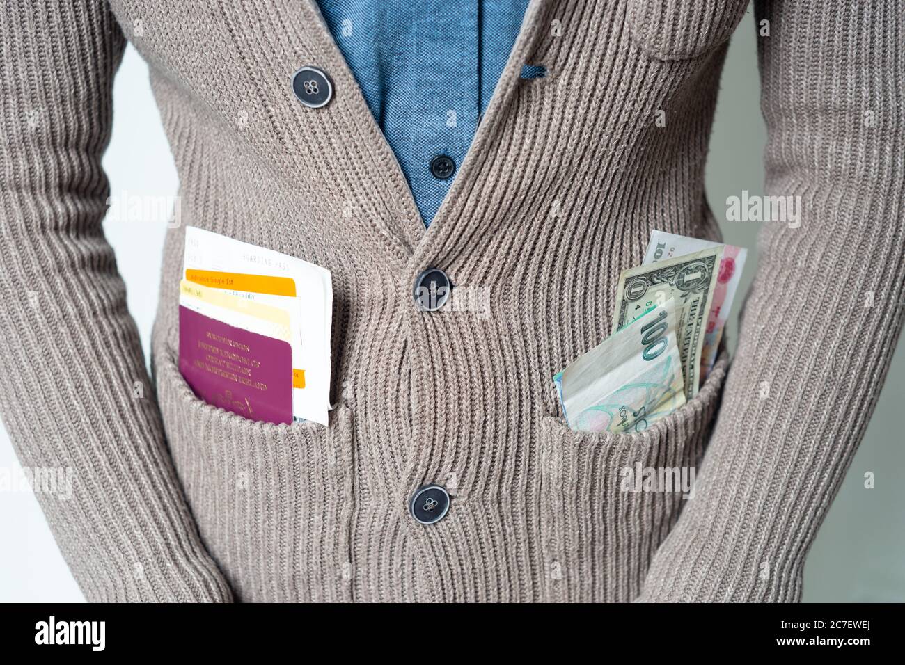 Young man wearing cardigan with passport and tickets and various currencies in pocket, concept - travel, traveller, worldwide Stock Photo