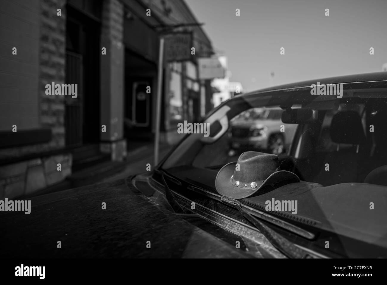 Horizontal greyscale shot of a cowboy hat in the car parked in the shadow on Route 66 street Stock Photo