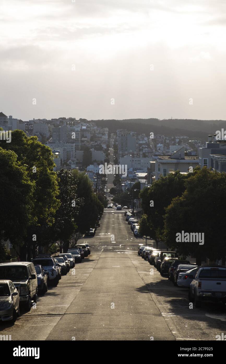 Vertical shot of a downhill road with cars parked on the sides under a ...