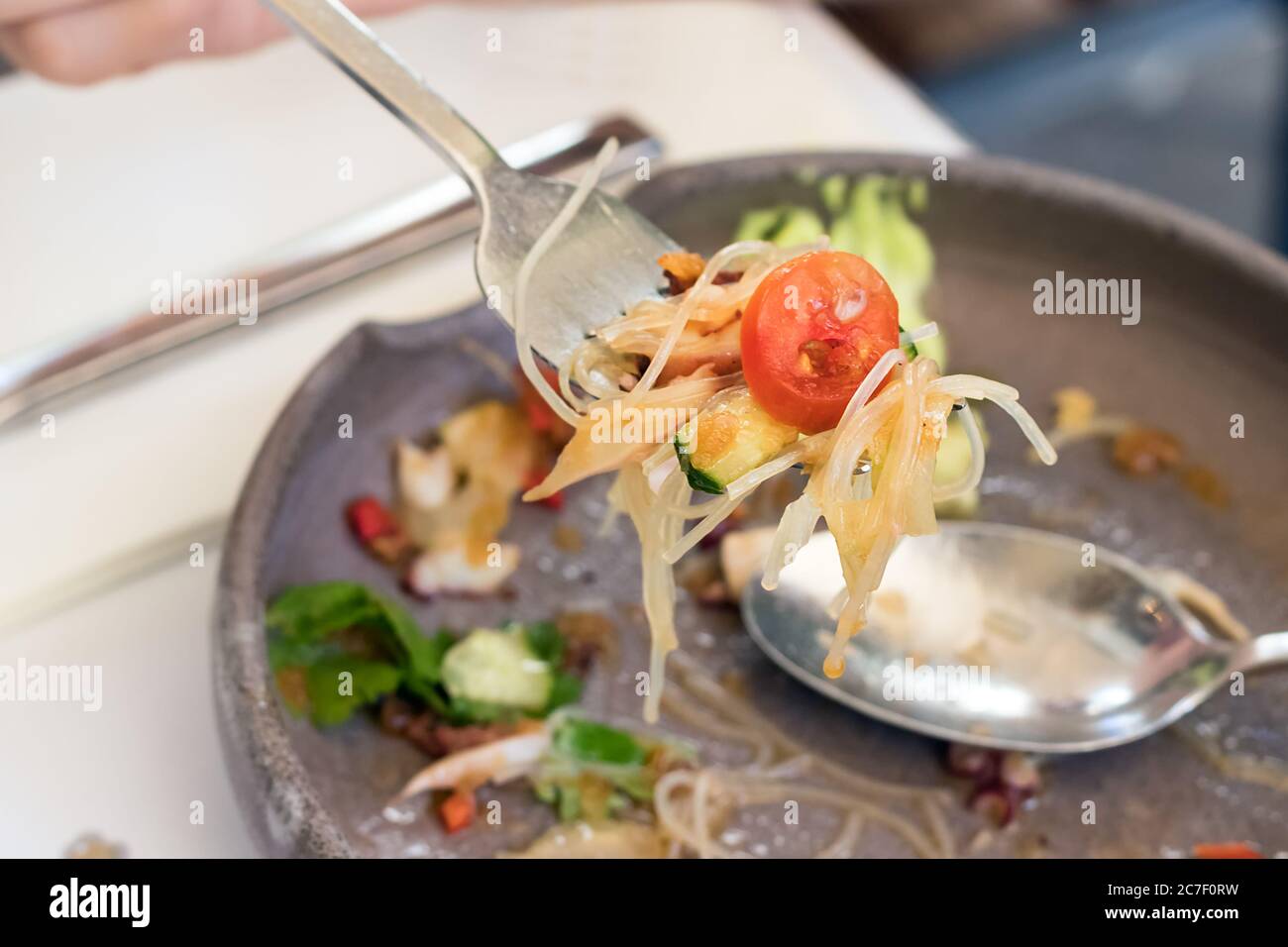Human hand holding a fork with food over a plate Stock Photo