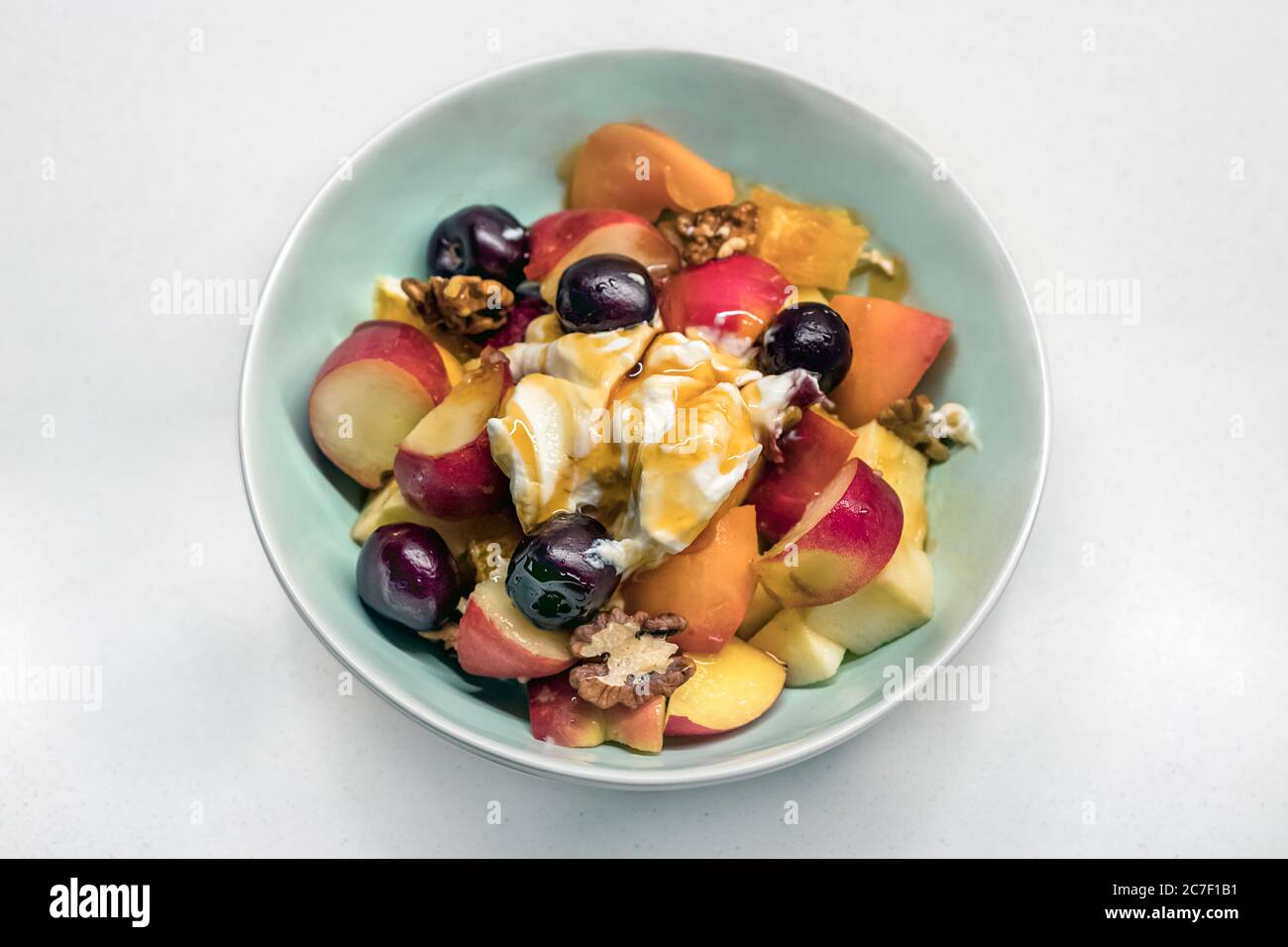 Top view of a home made greek fruit salad with nuts, apple, peach, grapes and yogurt with honey. Stock Photo