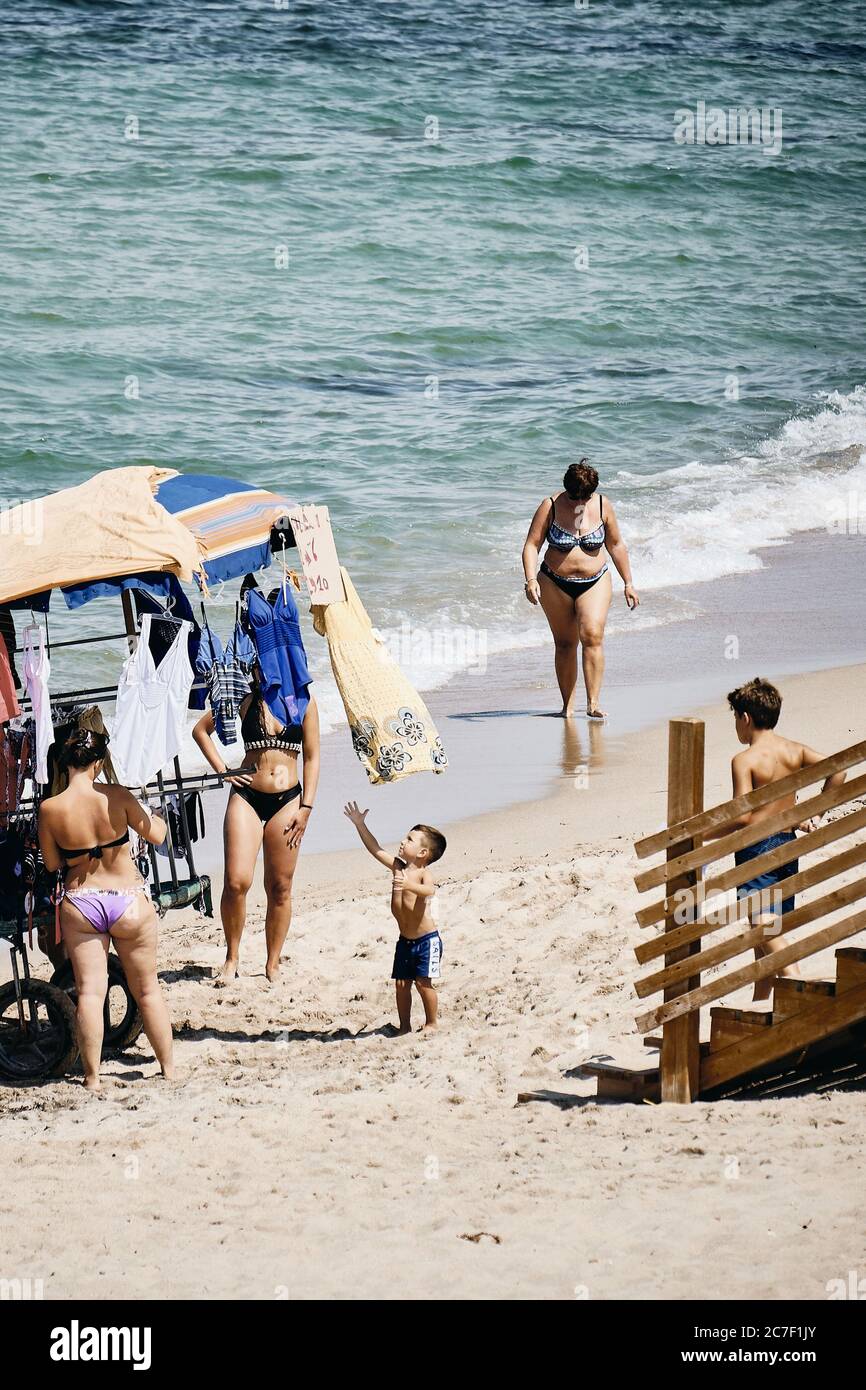 SPIAGGIA DI SAN PIETRO, ITALY - Aug 23, 2019: A toddler trying to catch a hanged beach dress from a booth cart on the beach at daytime Stock Photo