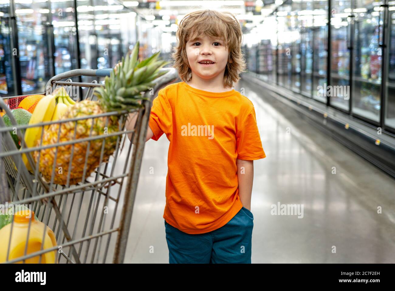 Funny boy with shopping cart full of fresh organic vegetables and