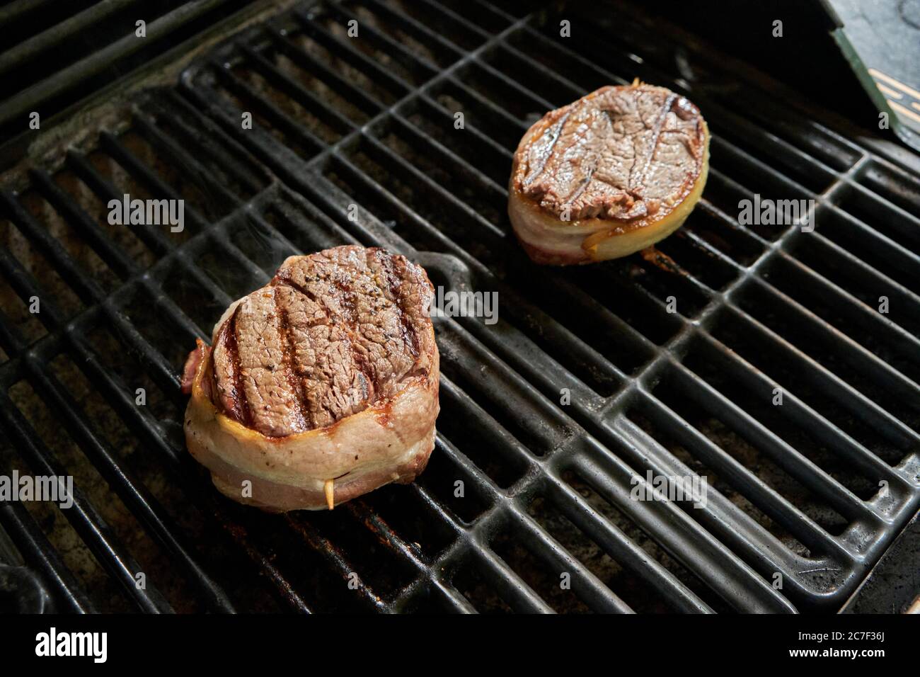 Thick filet steaks wrapped in bacon cooking on a gas barbecue grill