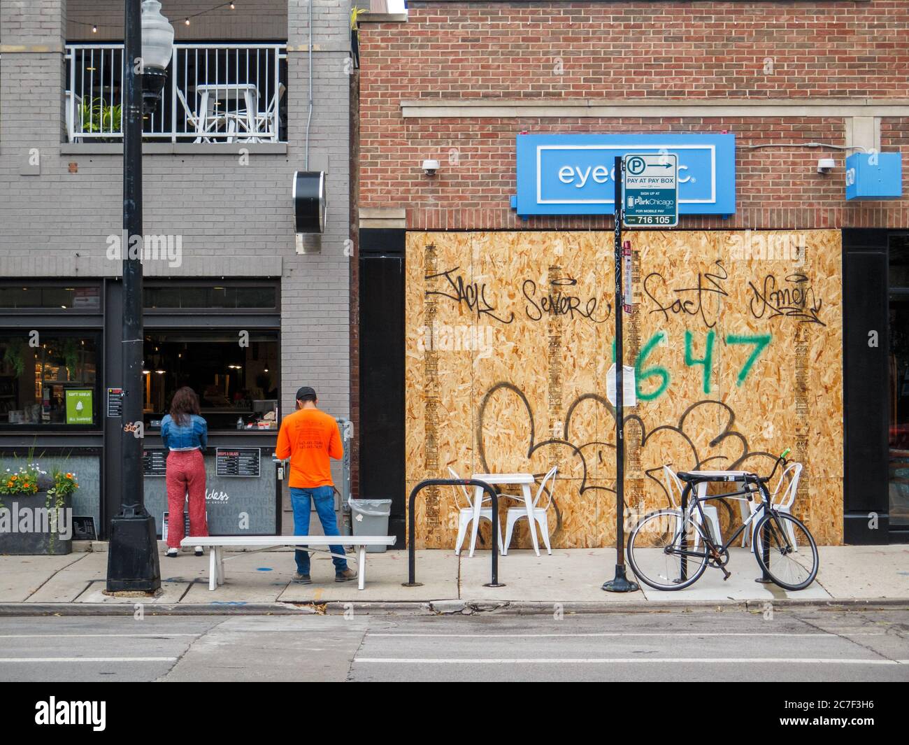 Boarded up storefront, result of recent civil unrest. Walk up café window with patrons. Bucktown neighborhood, Chicago, Illinois. Stock Photo