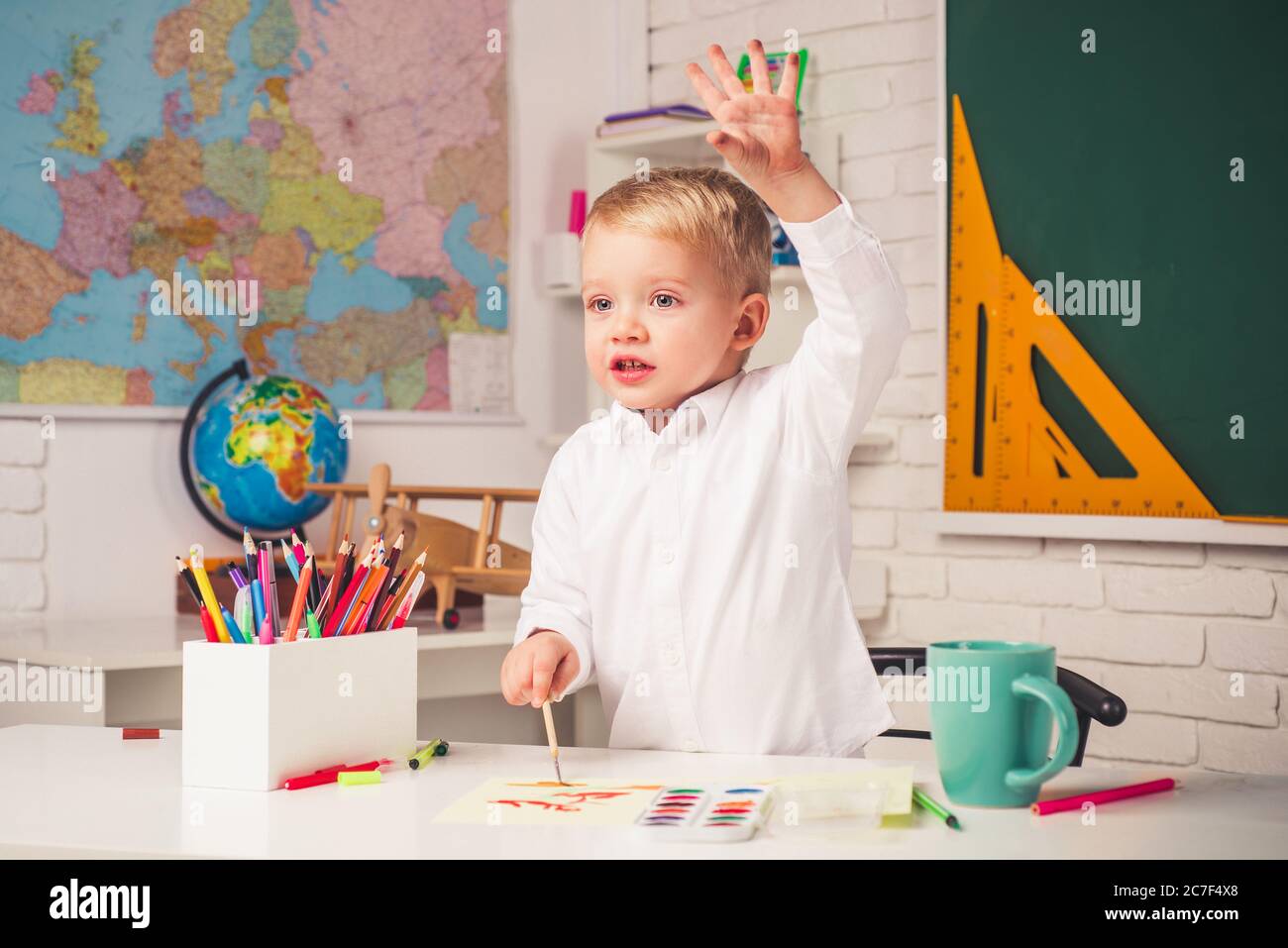 Happy cute industrious child is sitting at a desk indoors. Back to school. Home schooling. Talented child. Kid gets ready for school. Stock Photo