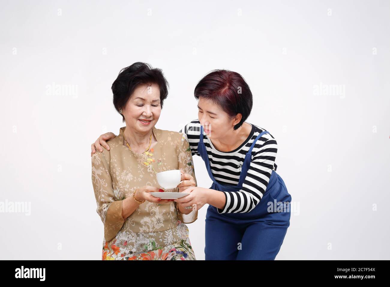 Senior woman drinking tea with her daughter take care, isolated on white background Stock Photo