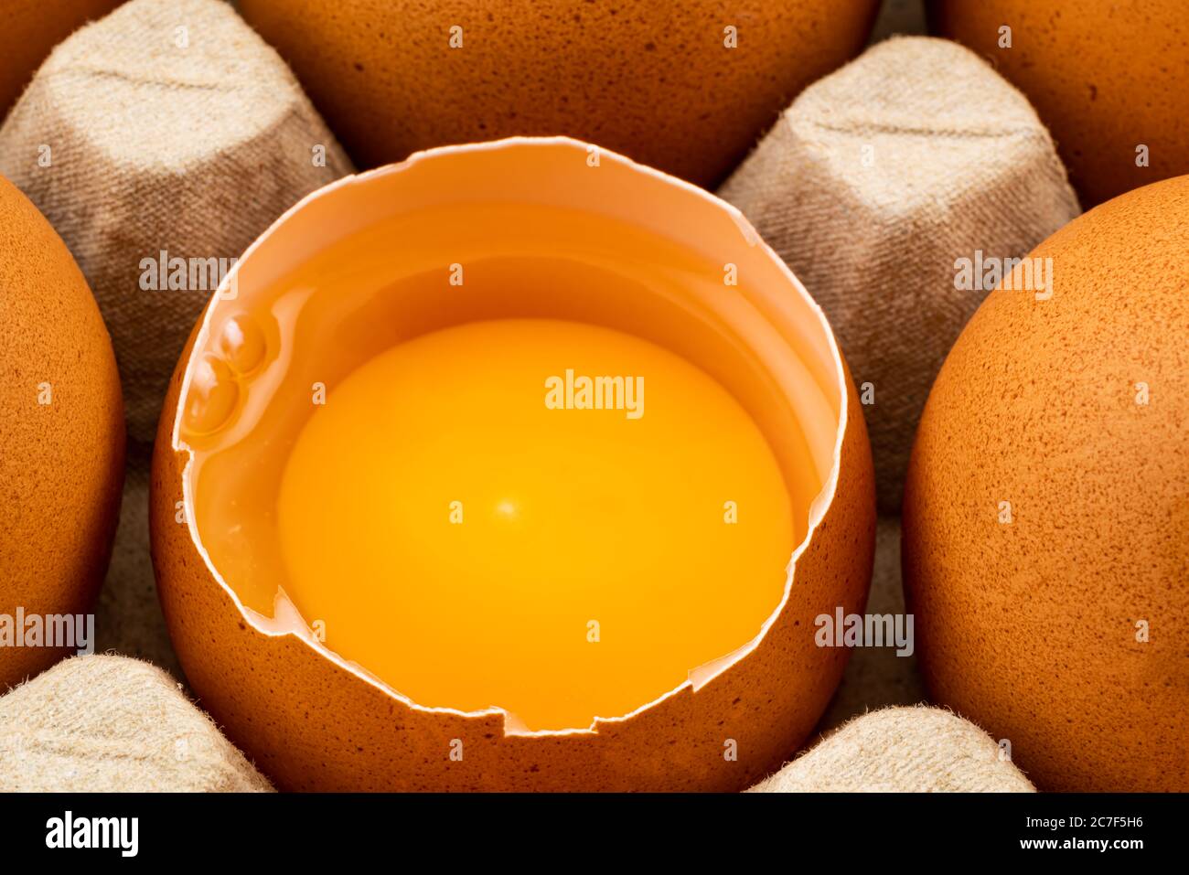 Half broken chicken egg and brown chicken eggs in egg carton on the table. Eggs are loaded with Choline, an important nutrient for the brain. Stock Photo