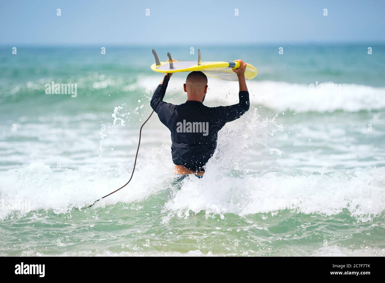 Surfer with surfboard goes into the ocean on a summer day. Sunny waves seascape Stock Photo