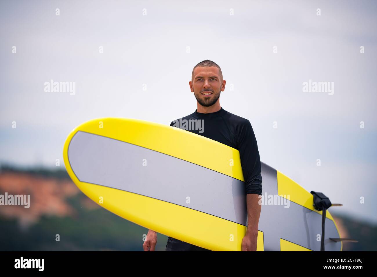 Surfer smiling, looking forward and holding surfboard on a sunny summer day. Stock Photo