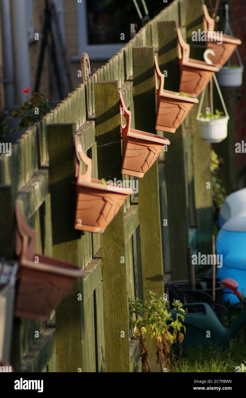A row of clay hanging baskets on a garden fence in the sunshine Stock