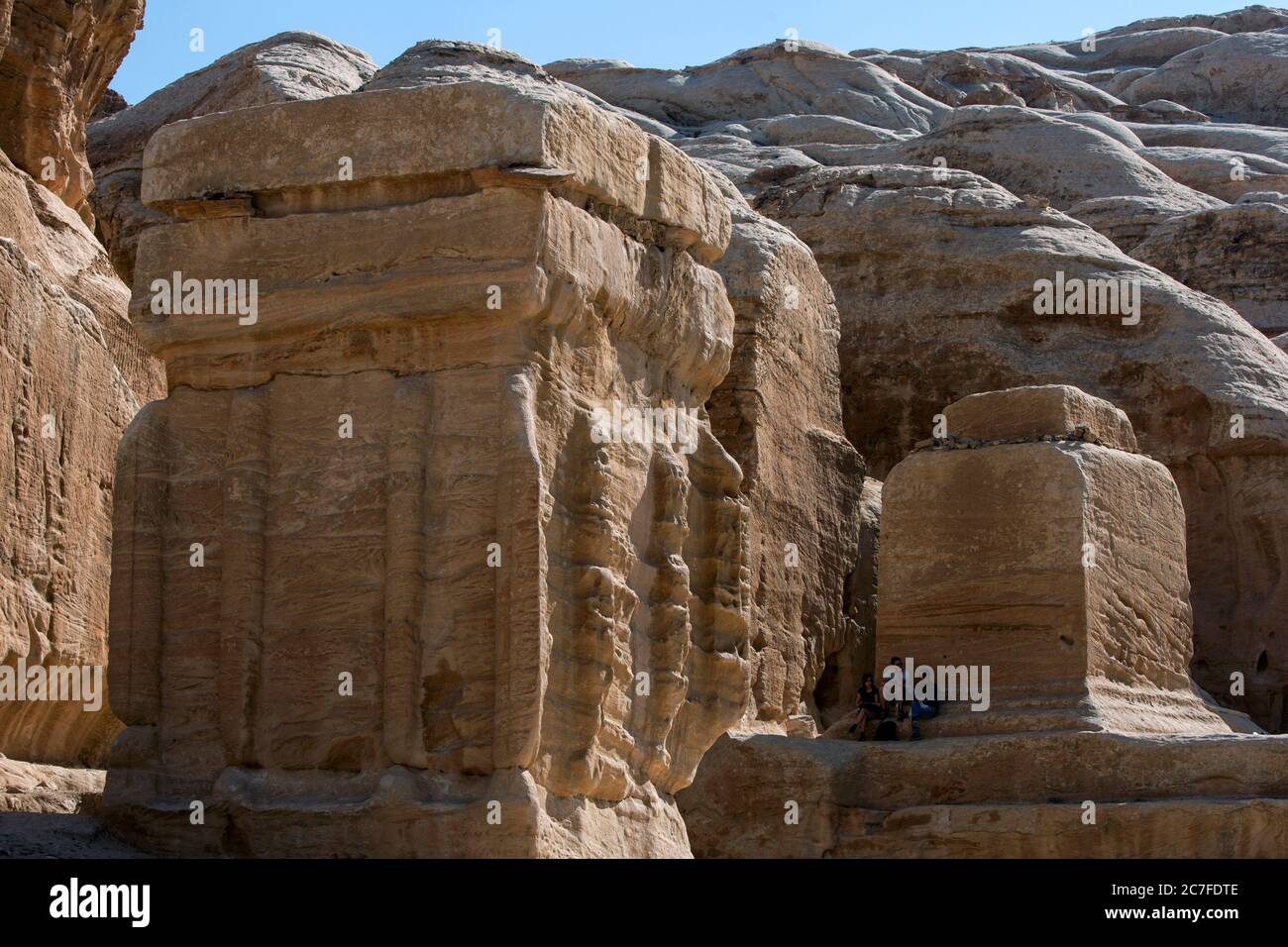 Tourists sit in the shade of giant carved boulders at the entrance of Petra in Jordan. Petra was possibly established as early as 312 BC. Stock Photo