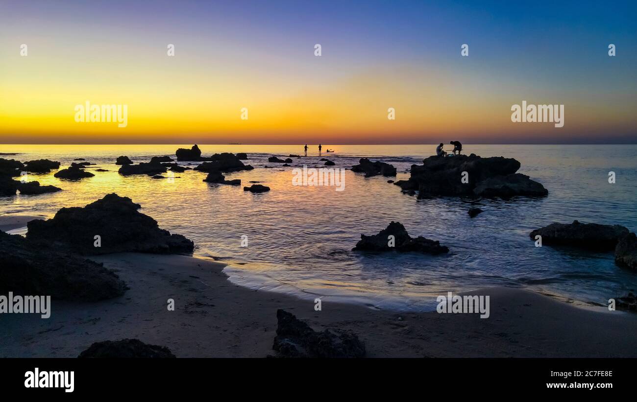 silhouettes of fishermen casting rods on a rocky beach at sunset Stock Photo