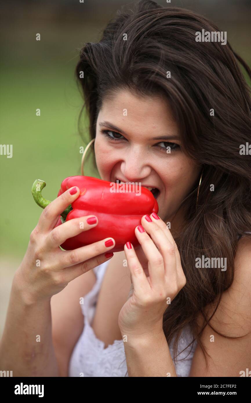 Young woman eats a whole red bell pepper Stock Photo