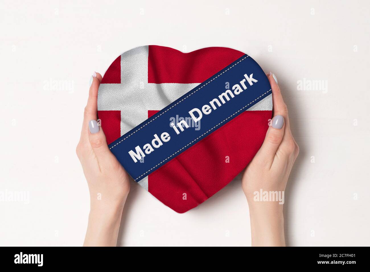 Inscription Made in Denmark the flag of Denmark. Female hands holding a heart shaped box. White background. Stock Photo