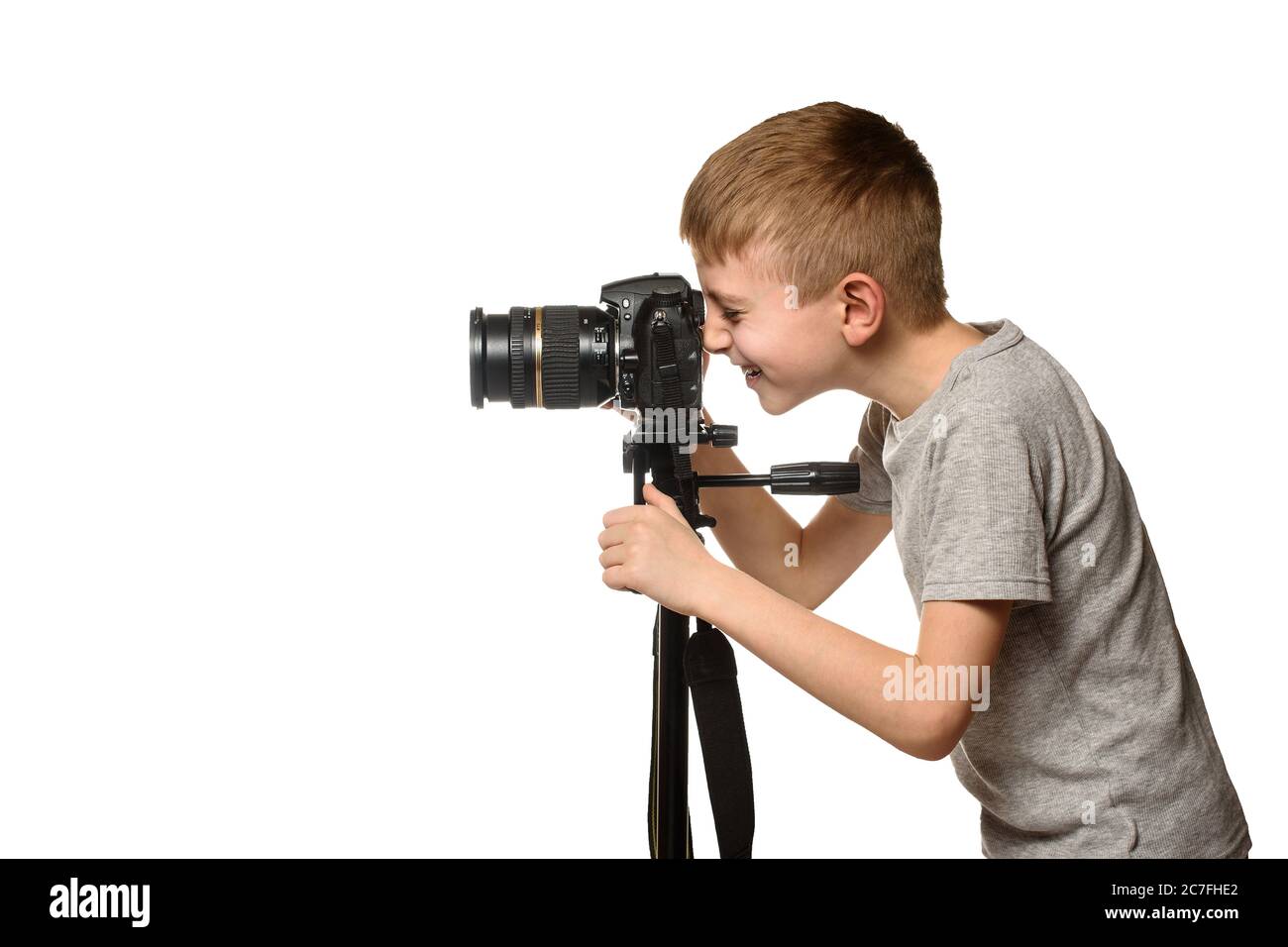 Smiling schoolboy takes pictures with a reflex camera. Side view. White background Stock Photo