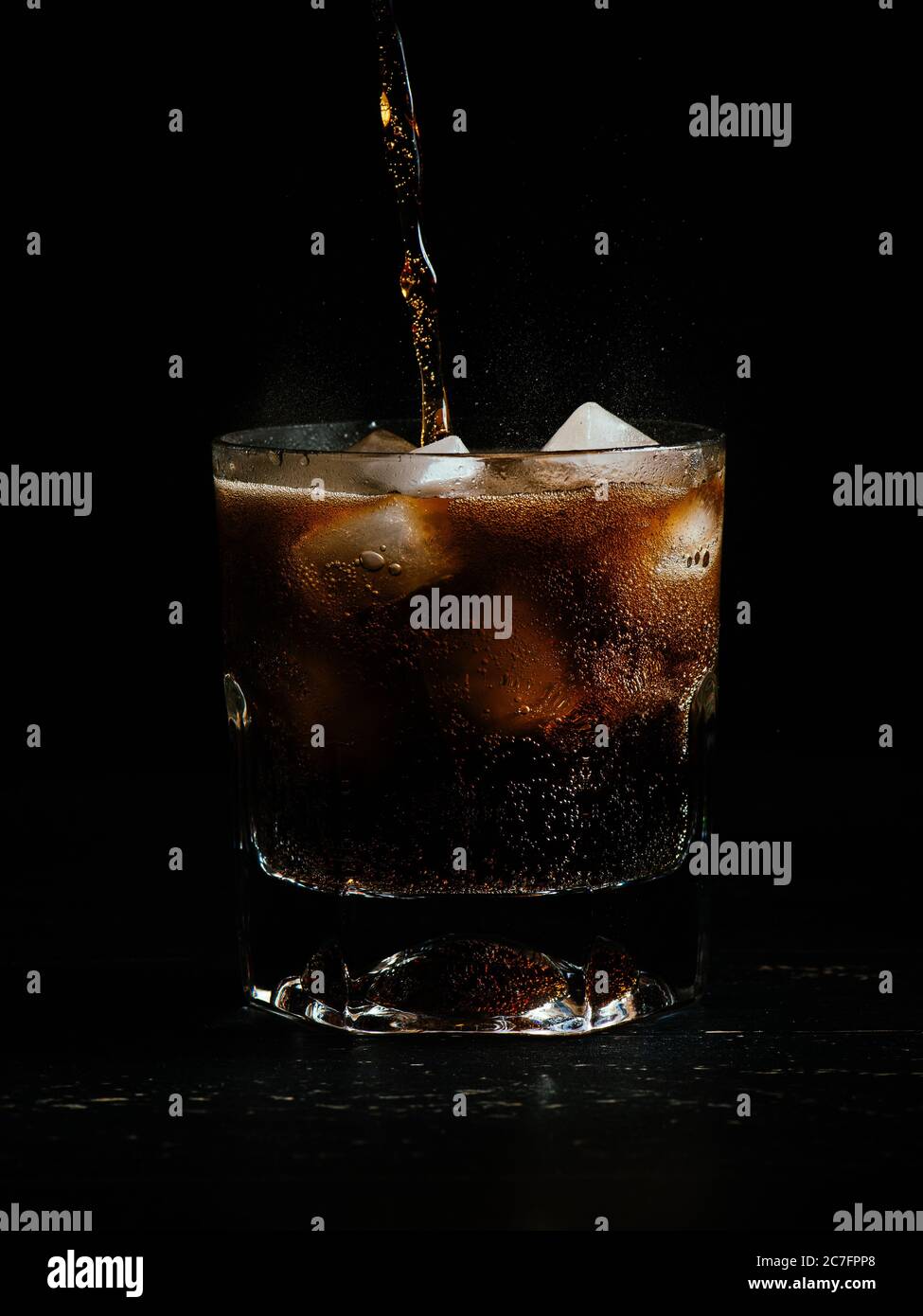 Vertical shot of coke being poured in a glass full of ice on a black ...