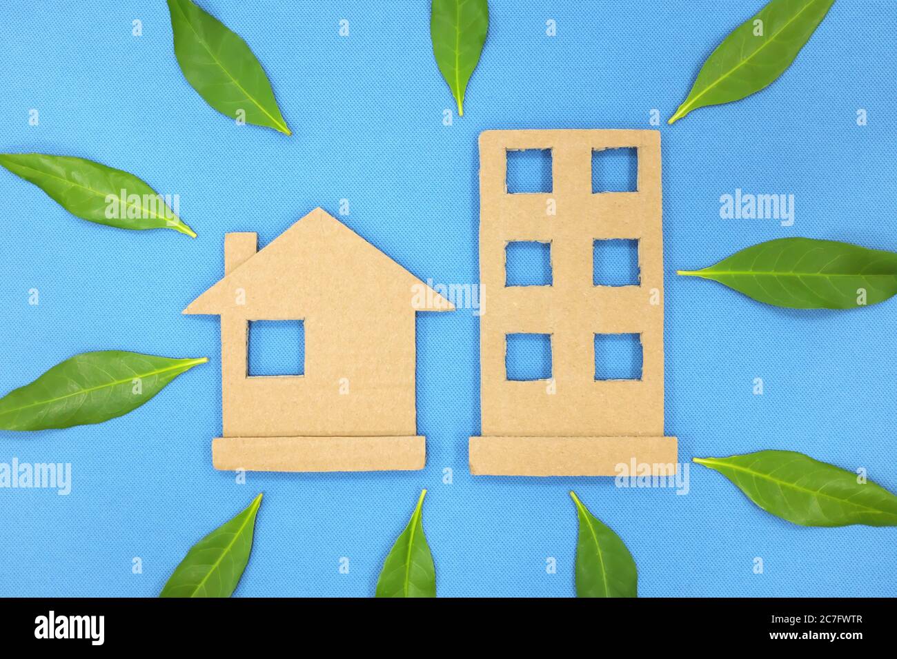 House and building cardboard cutout with fresh leaves. Green living community concept. Blue