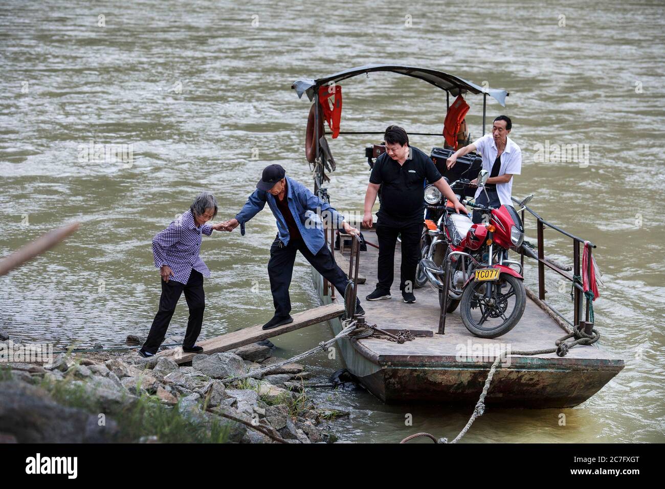 (200717) -- YANGXIAN, July 17, 2020 (Xinhua) -- Han Wenixn (2nd L) helps an elder board the boat at the Miaoshang crossing in Huangjinxia Town, Hanzhong City of northwest China's Shaanxi Province, July 16, 2020. Han Wenxin, 71, a ferryman for 60 years at the Miaoshang crossing, a 100-year-old crossing in Huangjinxia Town, stuck to his position every day despite of the weather and whenever the villagers needed him, and charged no money from his impoverished clients. In 2018, Han Wenxin broke his feet and called his son Han Baocheng back to continue his business. Although earning few money, Han Stock Photo