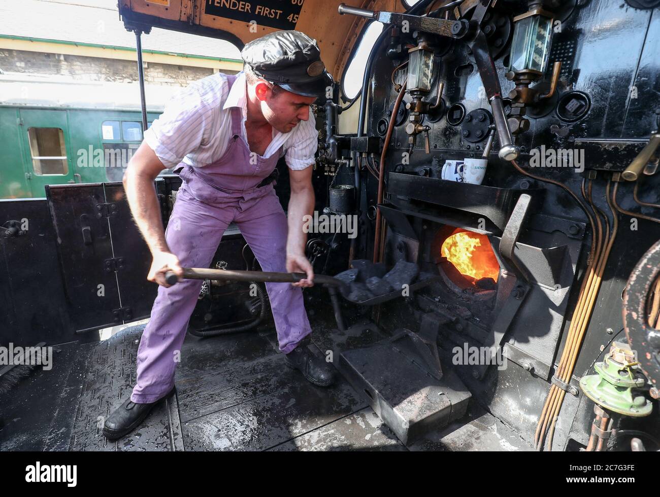 Fireman Alexander Atkins shovels coal into the firebox of the SR U Class steam locomotive No. 31806, as final preparations are made at the Swanage Railway ahead of the running of steam trains for the first time since the coronavirus lockdown in March. The heritage railway on the Isle of Purbeck, Dorset, will use steam engines again on Saturday with a non-stop service between Swanage and Norden stations with social distancing in place at stations and on trains and the wearing of face coverings. Stock Photo