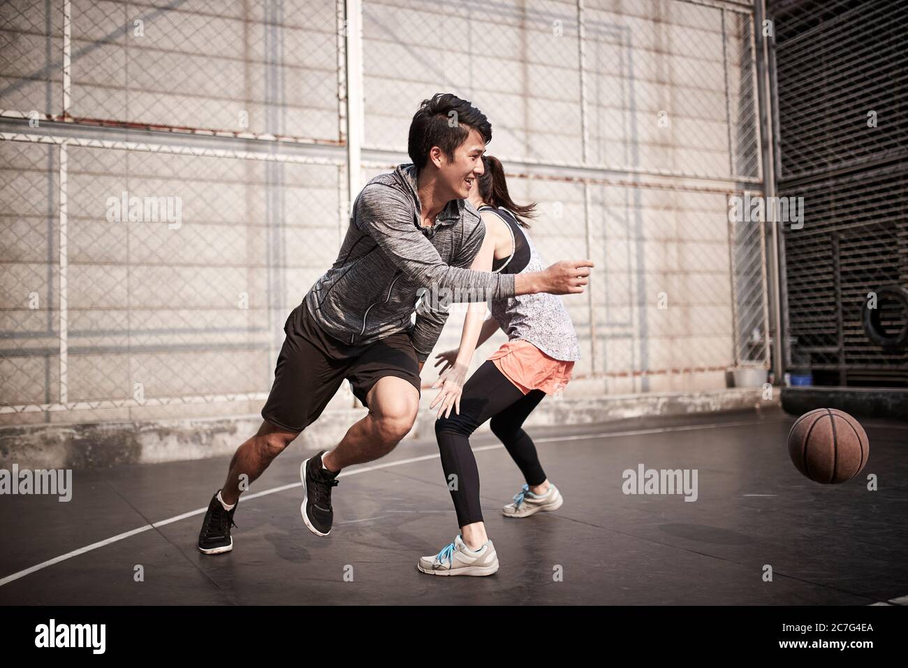 young asian adult man and woman having fun playing basketball on a outdoor court Stock Photo