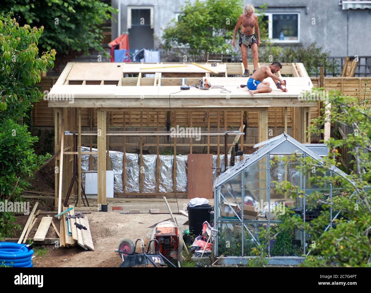 Two builders constructing the roof of a garden studio Stock Photo